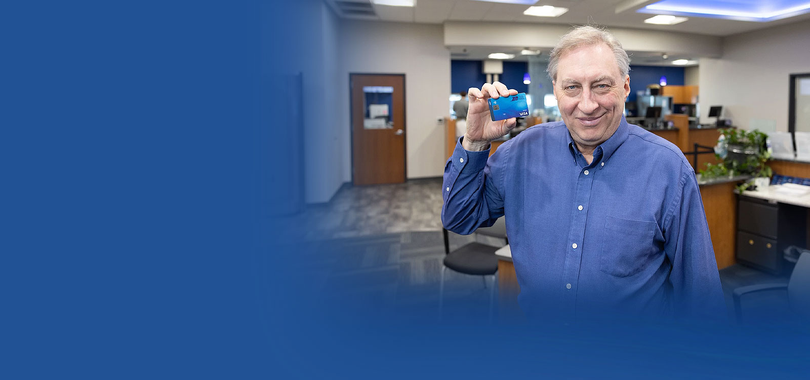 Man standing in an office holding an RCU debit card